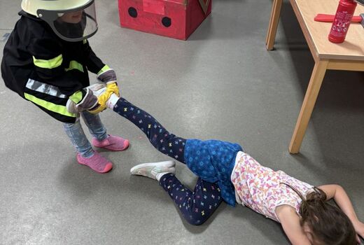 Ein Junge in Feuerwehrkleidung rettet ein Mädchen und zieht es über den Boden.