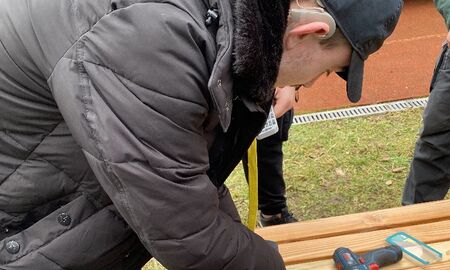 Ein junger Mann schraubt die Sitzfläche einer Bank fest