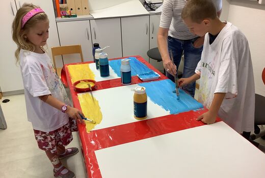 Kinder pinseln Farbe aufs Bild in blau und gelb