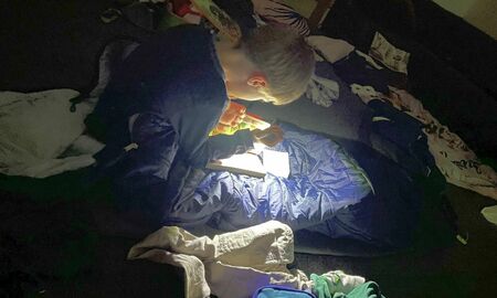 Ein Junge liest im Dunkeln mit einer Taschenlampe