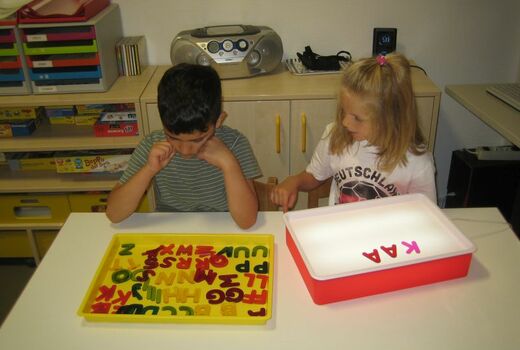 Zwei Kinder suchen aus vielen Buchstaben bekannte Buchstaben heraus und legen sie auf ein Leuchtfeld.
