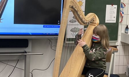 Eine Zweitklässlerin sitzt vorne vor der Tafel und zupft probeweise an einer Harfe.