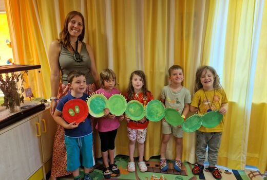Fünf Kinder und eine Lehrerin halten eine gebastelte Raupe vor sich.