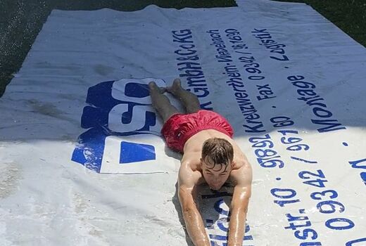 Ein großer Junge rutscht bäuchlings eine nasse LKW-Plane herunter.