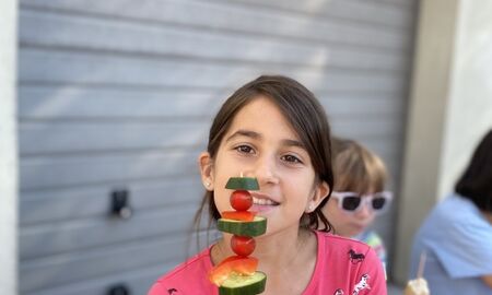 Ein Mädchen zeigt einen Spieß auf dem Gurken,Paprika und Tomaten stecken in die Kamera