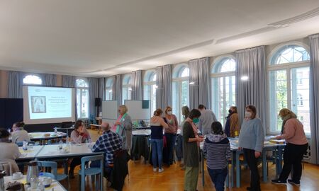 Besucher sitzen an Tischen, unterhalten sich oder stehen in Gruppen und tauschen sich aus