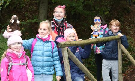 Sechs Kinder stehen auf einer Holzbrücke und halten die Maskottchen vom Freitagsclub hoch