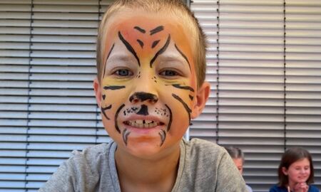 Ein Junge ist im Gesicht wie ein Tiger geschminkt und bemalt einen S