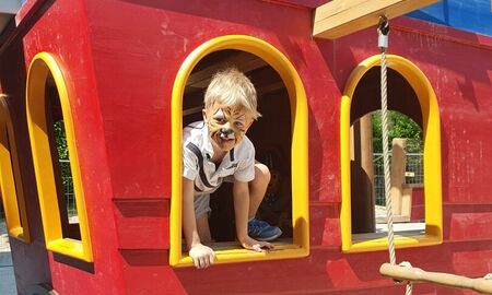 Ein kleiner Junge mit einem geschminkten Tigergesicht schaut aus dem Fenster eines Spielplatzpiratenschiffes