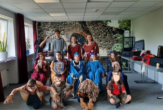 Die beiden Klassenlehrerinnen und elf Schüler und Schülerinnen posieren in mittelalterlichen Kostümen unter anderem als Ritter, gefährliche Tiere und feine Prinzen, Prinzessinnen und Hofmägde in einem Raum.