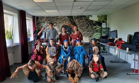 Die beiden Klassenlehrerinnen und elf Schüler und Schülerinnen posieren in mittelalterlichen Kostümen unter anderem als Ritter, gefährliche Tiere und feine Prinzen, Prinzessinnen und Hofmägde in einem Raum.