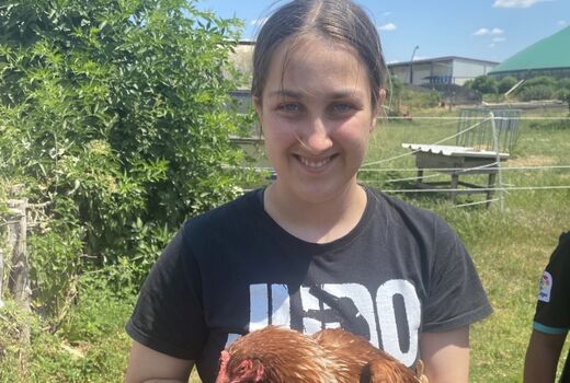 Ein Mädchen lacht in die Kamera. Es hat ein braunes Huhn auf dem Arm.