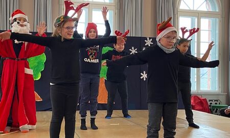 Abschlusstanz des Weihnachtstückes. Fünf Kinder strecken die Arme aus. Ein Kind ist als Weihnachtsmann verkleidet
