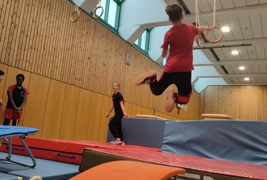 Ein Junge ist von einem orangefarbenen Sprungbrett abgesprungen und versucht die Ringe zu greifen.