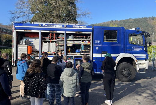 Zwölf Schüler stehen vor einem Fahrzeug des THW. Ein Mitarbeiter des THW erklärt etwas.