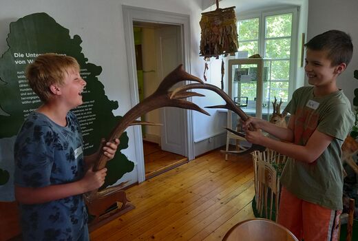 Zwei Viertklässler halten jeweils ein Geweih in den Händen, stehen sich gegenüber und kämpfen damit spielerisch und lachend gegeneinander.