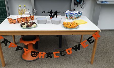 Auf einem mit Happy Halloween Girlande dekorierten Tisch stehen Essen und Getränke mit gruseligen Gesichtern.