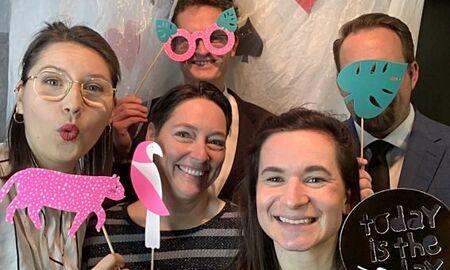 fünf Erwachsene vor einer Fotowand mit Masken