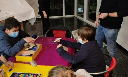 Drei SchülerInnen bemalen Steine. Sie sitzen an einem Tisch. Herr Ulrich steht daneben.