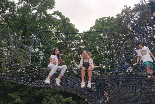 Das Kletternetz: Im Vordergrund sitzen zwei Mädchen. Sie lächeln und machen das Victory-Zeichen.