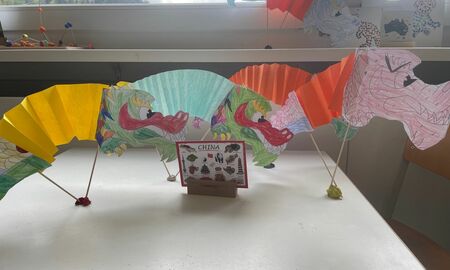 Auf einem Tisch steht eine bildliche Informationskarte zum Land China. Daneben und dahinter stehen fünf gebastelte Drachen mit Ziehharmonika-Körper.