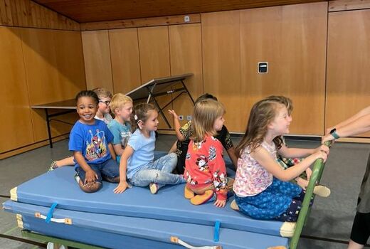 Acht Kinder sitzen auf einem Mattenwagen und spielen Feuerwehreinsatz.