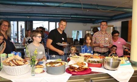 Kinder und Erwachsene stehen mit Tellern in den Händen hinter einem Buffet