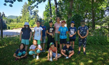 Lehrerin posiert mit 3 Schülerinnen und 9 Schülern für ein Gruppenfoto auf einer Wiese unter einem Baum