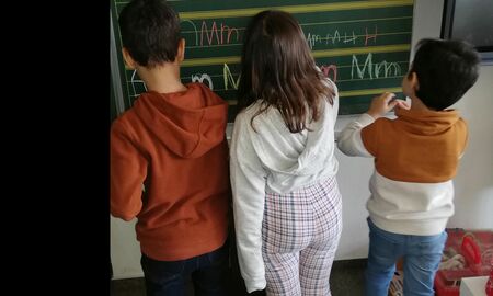 Drei Kinder stehen nebeneinander an der Tafel und schreibe das M in Groß- und Kleinbuchstaben an die Tafel.