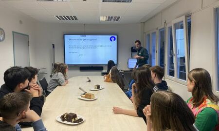 Eine Gruppe Jugendlicher sitzt an einem Tisch und schaut auf ein interaktives Panel