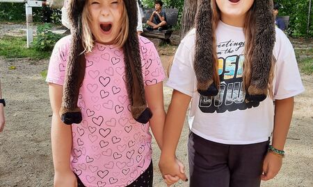 Zwei Schülerinnen posieren fröhlich mit Wildschwein-Mützen auf dem Kopf und halten sich an den Händen. Sie haben jeweils ein Bein zusammengebunden, sodass sie diese nur gemeinsam bewegen können.