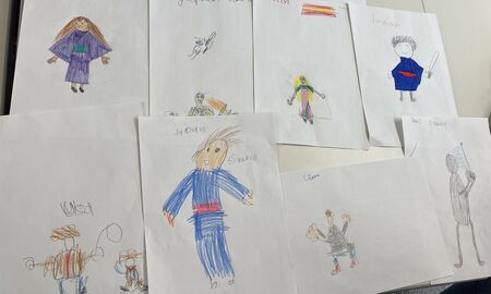 Auf einem Tisch liegen Kinderzeichnungen von Menschen mit traditioneller Kleidung aus unterschiedlichen Ländern wie beispielsweise Japan, USA und Spanien. Oben liegt ein Blatt mit der Überschrift: Traditionelle Kleidung weltweit.