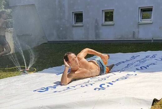 Ein Mann rutscht in Seithaltung die nasse LKW-Plane herunter.