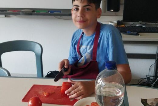 Ein Junge schneidet Paprika. Er hält inne und lächelt in die Kamera.