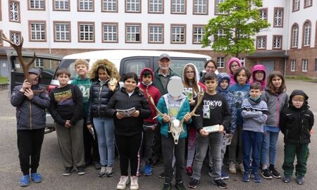 Ein Gruppenfoto mit 16 Kindern und einem Jäger. Drei Kinder halten Geweihe.