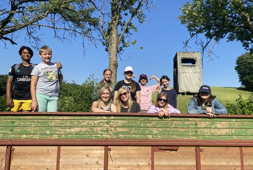 Acht SchülerInnen und zwei Lehrerinnen lachen in die Kamera. Hinter ihnen sind Felder.