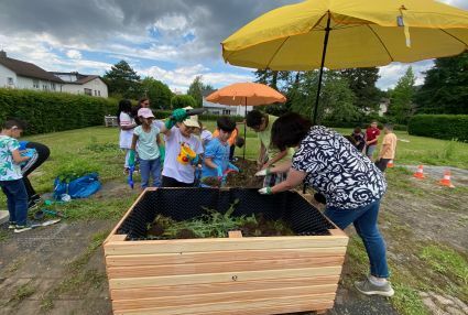 Kinder befüllen ein Hochbeet mit Grunschnitt