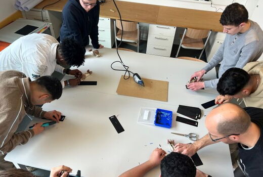 Blick von oben auf einen Werkzeugtisch, an dem 8 Menschen bauen.