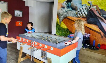 Zwei Jungen und ein Mädchen spielen in einem Raum Tischfußball an einem Tischkicker.