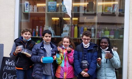 Fünf Kinder stehen vor dem Schaufenster des Unverpacktladens und zeigen die Behältnisse mit ihren Einkäufen