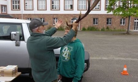 Ein Jäger hält einem Jungen ein Hirschgeweih an den Kopf