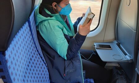 Ein Mädchen sitzt im Zug am Fenster und liest in einem Buch