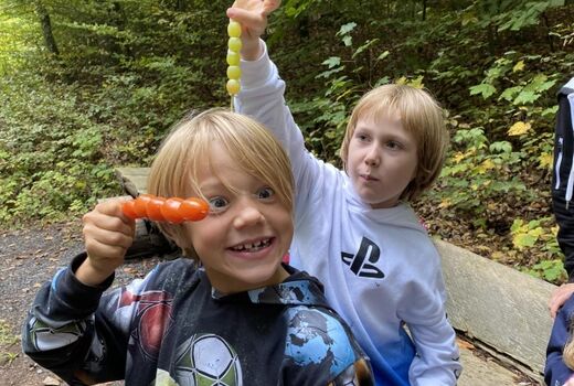 Die Gemüsespieße sind mal wieder bunt und lecker. Zwei Kinder halten einen Trauben und einen Tomatenspieß.