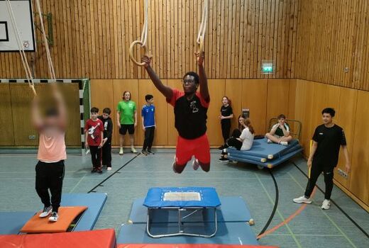 In einer Turnhalle schwingt ein Jugendlicher an den Ringen.