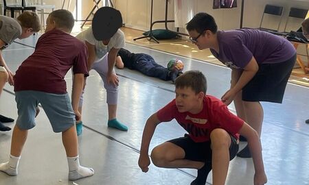 Fünf Schüler bewegen sich gebeugt vorwärts. Ein Kind liegt auf dem Bauch und mit einem Ball auf den Füßen im Hintergrund auf dem Boden.