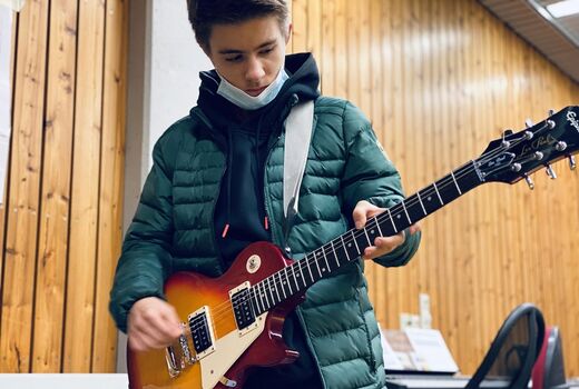 Ein Schüler steht mit einer Gitarre umgehängt und spielt auf der Gitarre