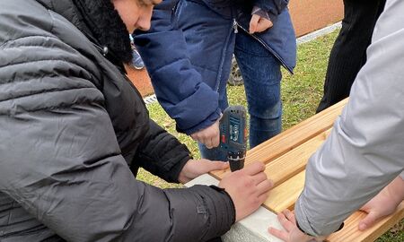 Ein junger Mann schraubt die Sitzfläche einer Bank fest