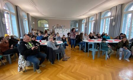 Viele Menschen sitzen an Tischen im Speisesaal und warten auf den Auftritt der Schüler*innen