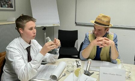 Ein Junge, am Kopfende des Tisches, spricht in ein Mikrofon