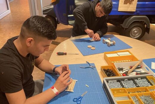 Zwei Schüler mit Bauteilen in der Hand an einem Tisch voll Werkzeug und Kleinteile